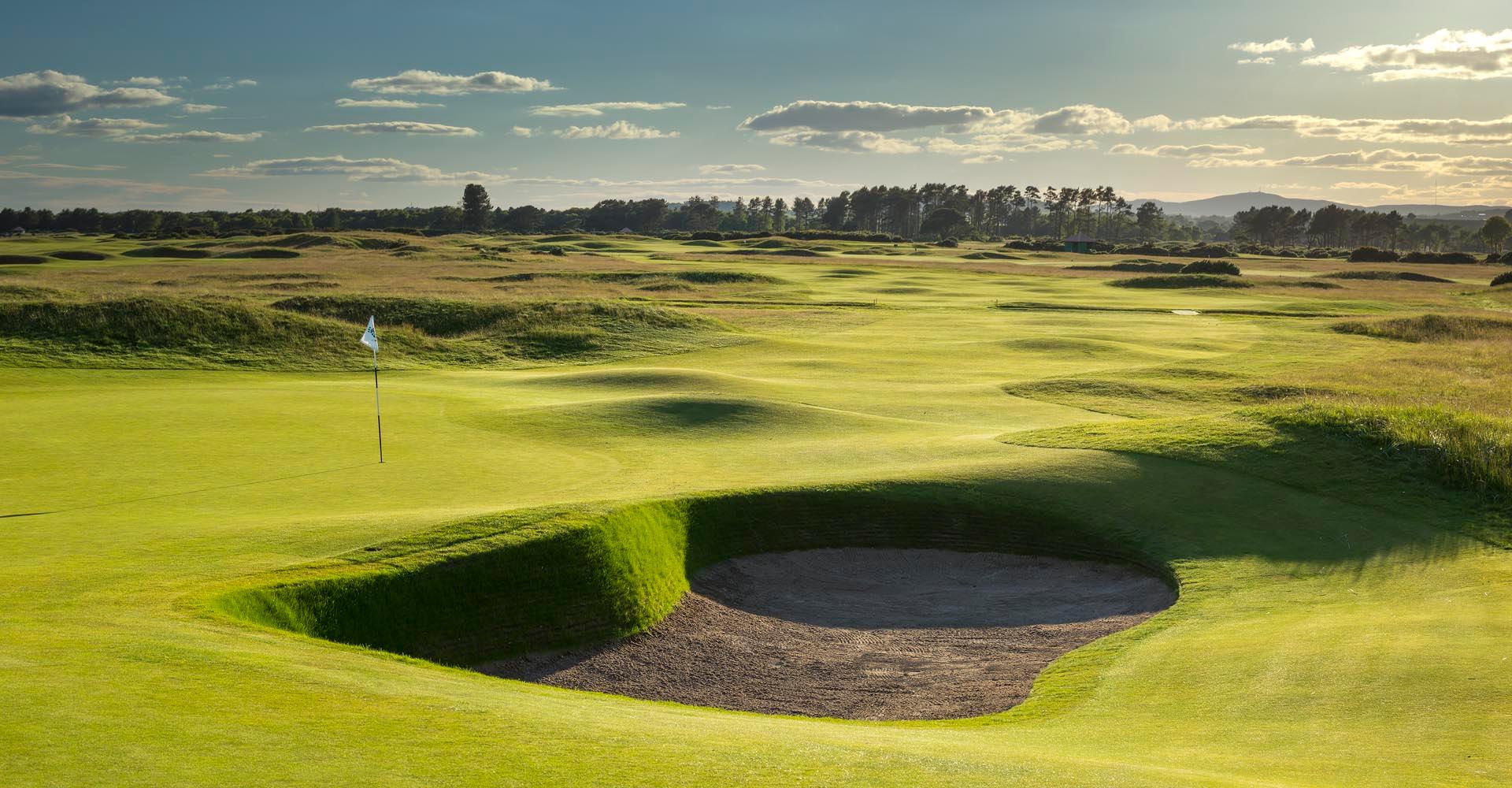 A well maintained fairway leading to a smooth green next to a sand bunker in Scotland