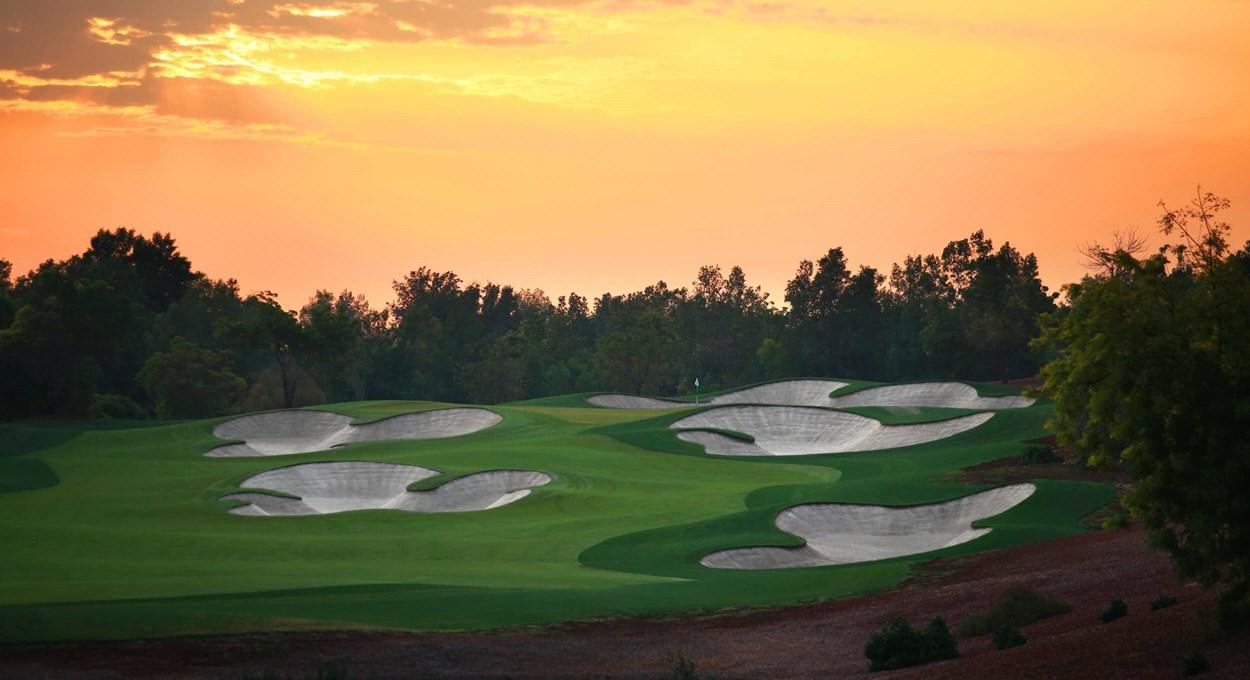 A smooth Dubai green surrounded by sand bunkers at sunset