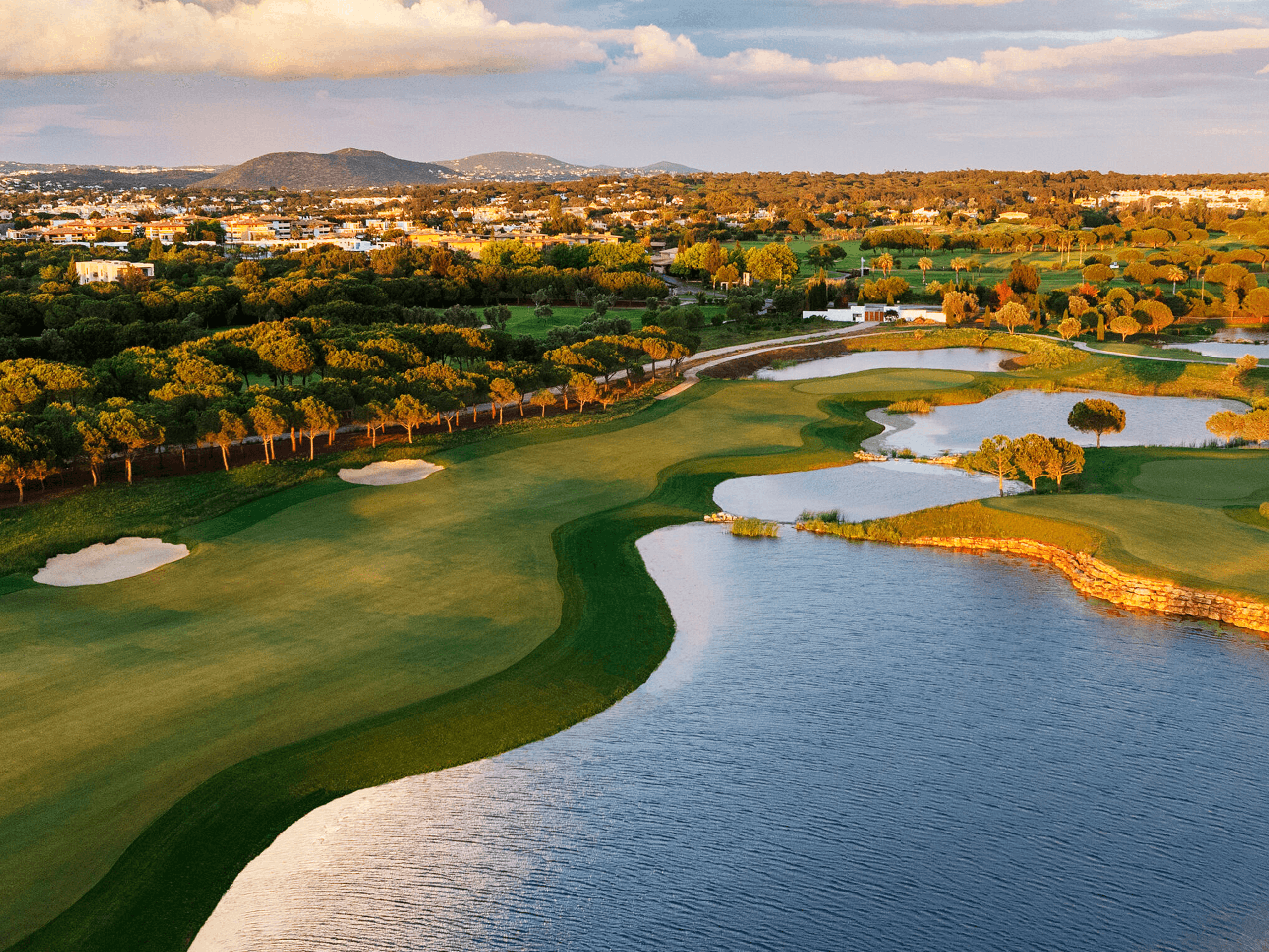 A well maintained fairway nestled with sand bunkers next to a water hazard